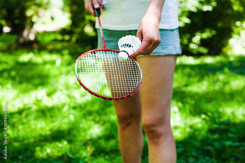 Young woman in white t-shirt and denim shorts playing badminton in the park in sunny day. Healthy lifestyle concept. Fitness concept.