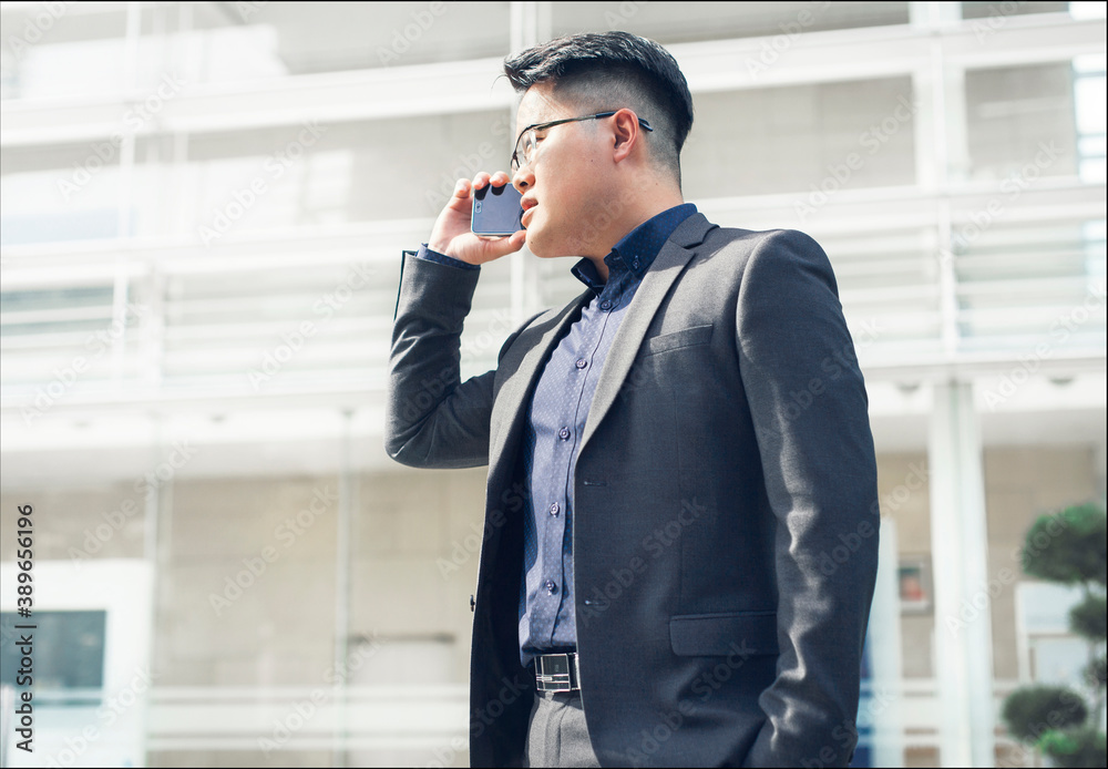 Young businessman talking on smartphone outside building on sunny day - business finance concept Young businessman talking on smartphone outside building on sunny day - business finance concept