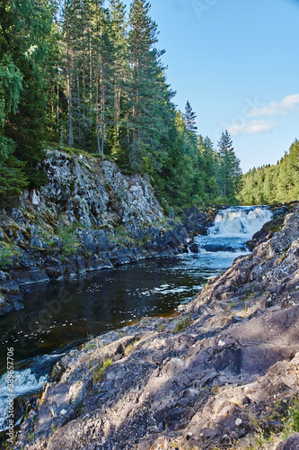 Plain waterfall Kivach.Long multistage flat waterfall. Seething waves and water falling on stones are visible. The slopes are rocky, spray and rainbow are visible. Russia, Karelia, Kivach