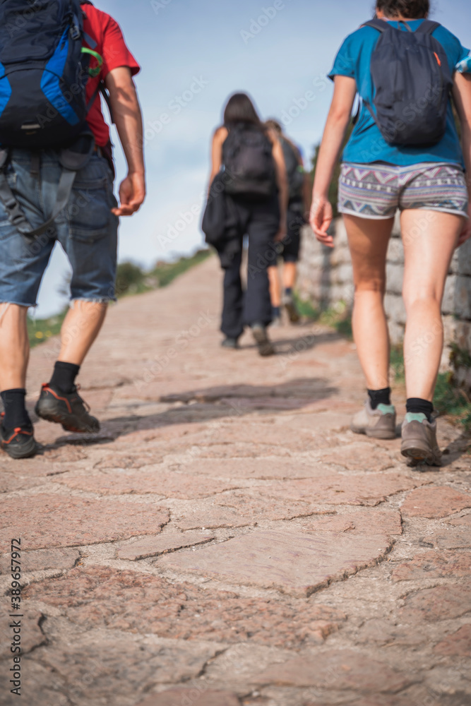 In the foreground a stone road, focused, and in the background three people Backpacker, not focused, walking.