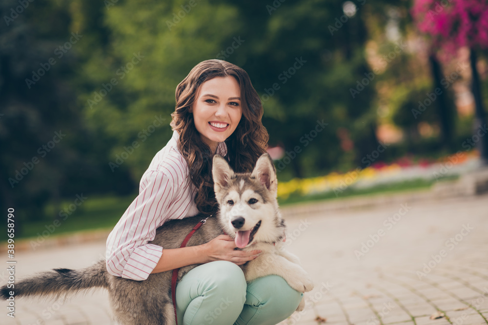 Photo of charming positive curly hair woman hug favorite lovely pet dog wear striped shirt green pants in park outdoors Photo of charming positive curly hair woman hug favorite lovely pet dog wear striped shirt green pants in park outdoors