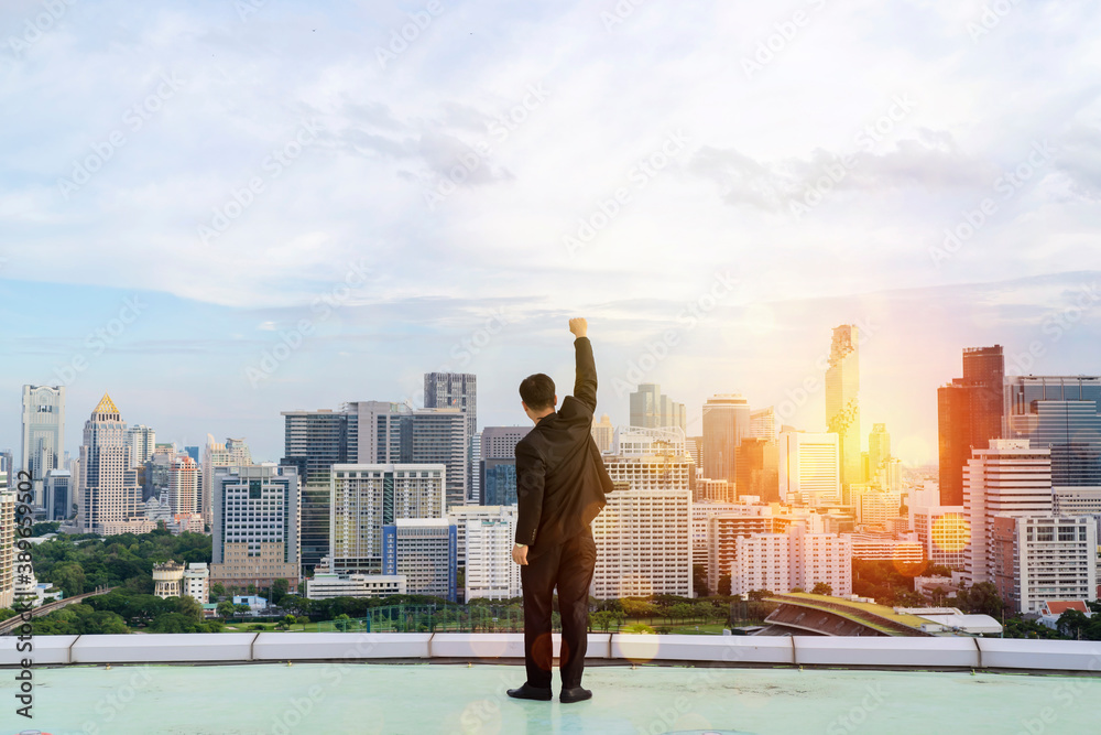 Businessman standing on a roof and looking at city, Raise your hands to express your joy in your accomplishments. Businessman standing on a roof and looking at city, Raise your hands to express your joy in your accomplishments.