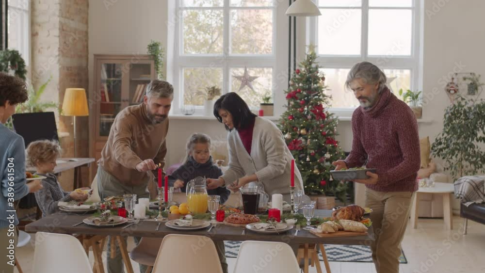 PAN shot of happy family setting Christmas table together. They are putting dishes on dinner table and lighting candles. Christmas tree in background PAN shot of happy family setting Christmas table together. They are putting dishes on dinner table and lighting candles. Christmas tree in background