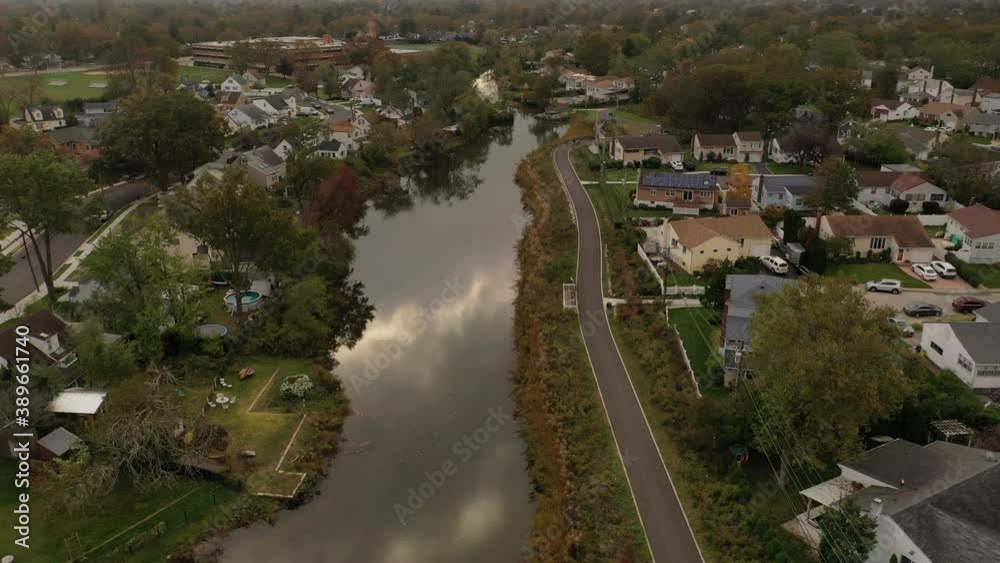 An aerial drone flight over a reflective pond on a cloudy afternoon. The camera dolly in & slowly tilt up to reveal the horizon. The calm scene shows a grey, cloudy sky with a golden hue from the sun. An aerial drone flight over a reflective pond on a cloudy afternoon. The camera dolly in & slowly tilt up to reveal the horizon. The calm scene shows a grey, cloudy sky with a golden hue from the sun.