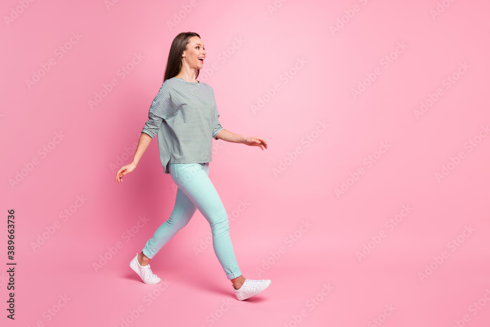 Full size profile photo of optimistic pretty woman going wear blue trousers sneakers shirt isolated on pink color background Full size profile photo of optimistic pretty woman going wear blue trousers sneakers shirt isolated on pink color background
