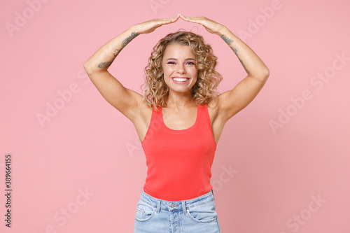 Smiling cheerful beautiful young blonde woman 20s wearing casual tank top standing holding hands above head like roof of head looking camera isolated on pastel pink colour background  studio portrait.