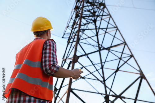 Electrical engineer with walkie talkie near high voltage tower, low angle view photo