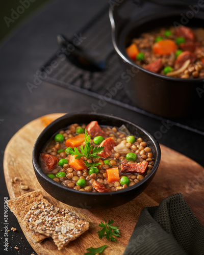 Traditional Spanish dish of lentil stew with chorizo and potatoes on a dark background, mediterranean food recipe. Selective focus.