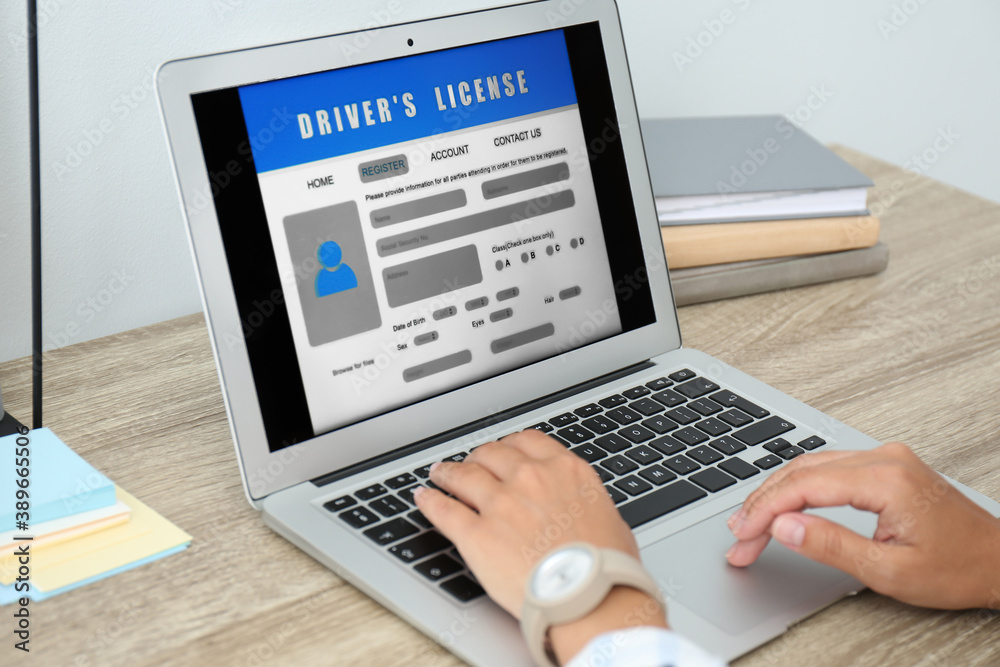 Woman using laptop to fill driver's license application form at table in office, closeup Woman using laptop to fill driver's license application form at table in office, closeup