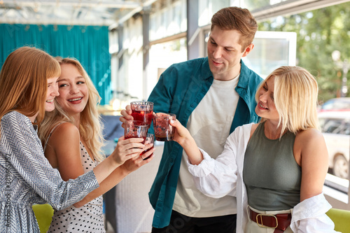 group of young caucasian people celebrating birthday with clinking glass of beverage, women and man gathered in restaurant for congratulating birthday man