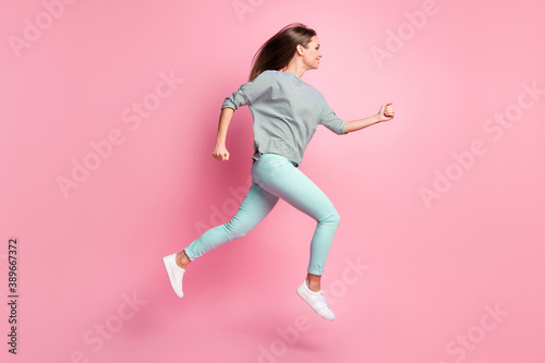 Full size profile photo of sweet long hair girl jumping run hands fists wear shirt blue pants white sneakers isolated on pink background