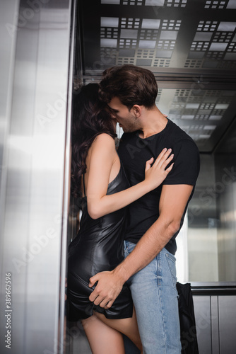 Man in black t-shirt and jeans touching buttock of curly woman in elevator