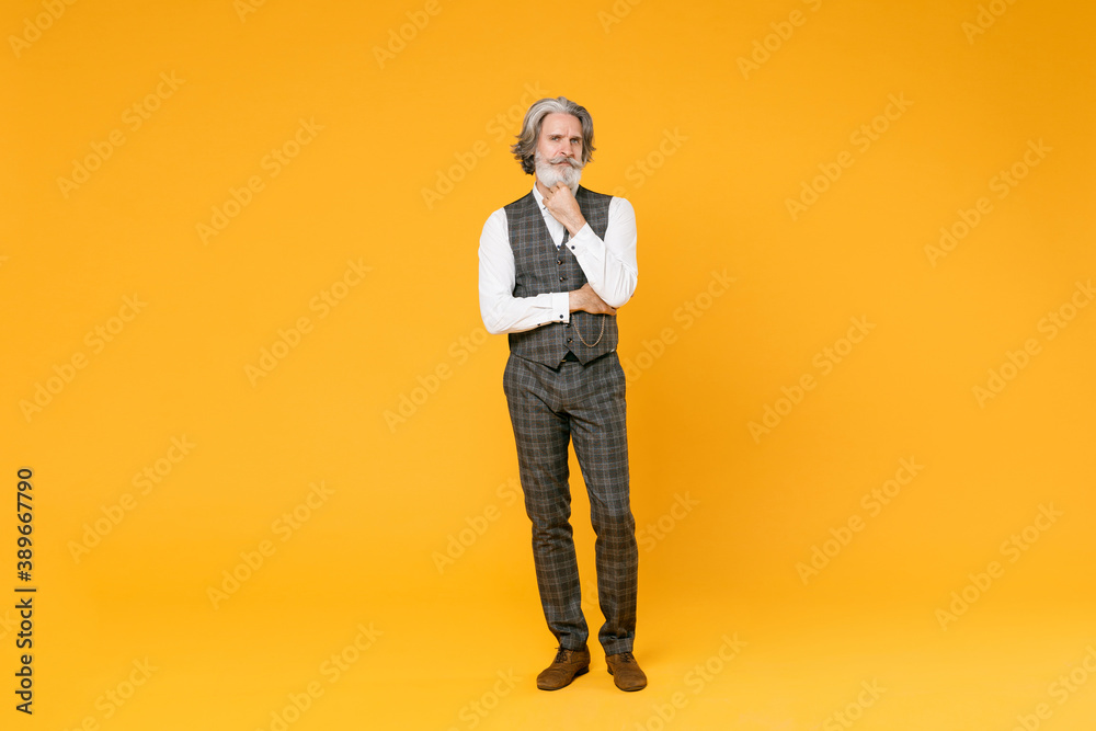 Full length puzzled elderly gray-haired business man in checkered suit waistcoat white shirt put hand prop up on chin isolated on yellow background studio portrait. Achievement career wealth concept. Full length puzzled elderly gray-haired business man in checkered suit waistcoat white shirt put hand prop up on chin isolated on yellow background studio portrait. Achievement career wealth concept.
