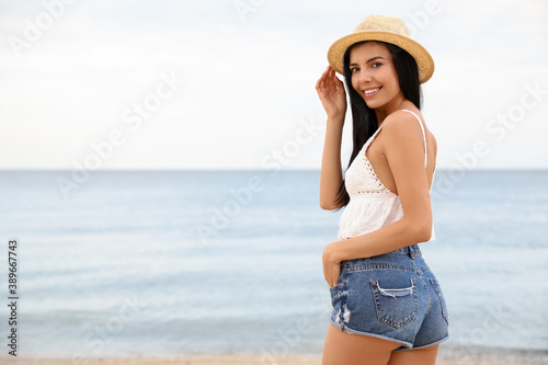 Beautiful young woman with beach hat near sea. Space for text