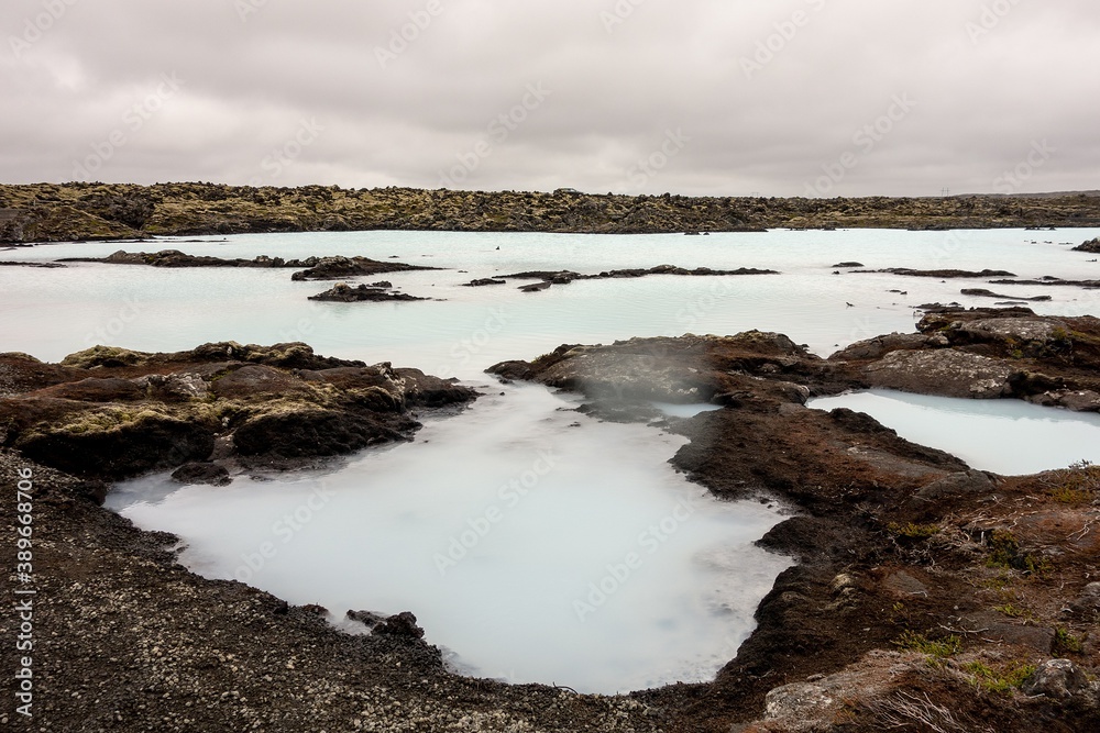Milky white waters of Icelandic thermal nature bath with black volcanic rocks near blue lagoon