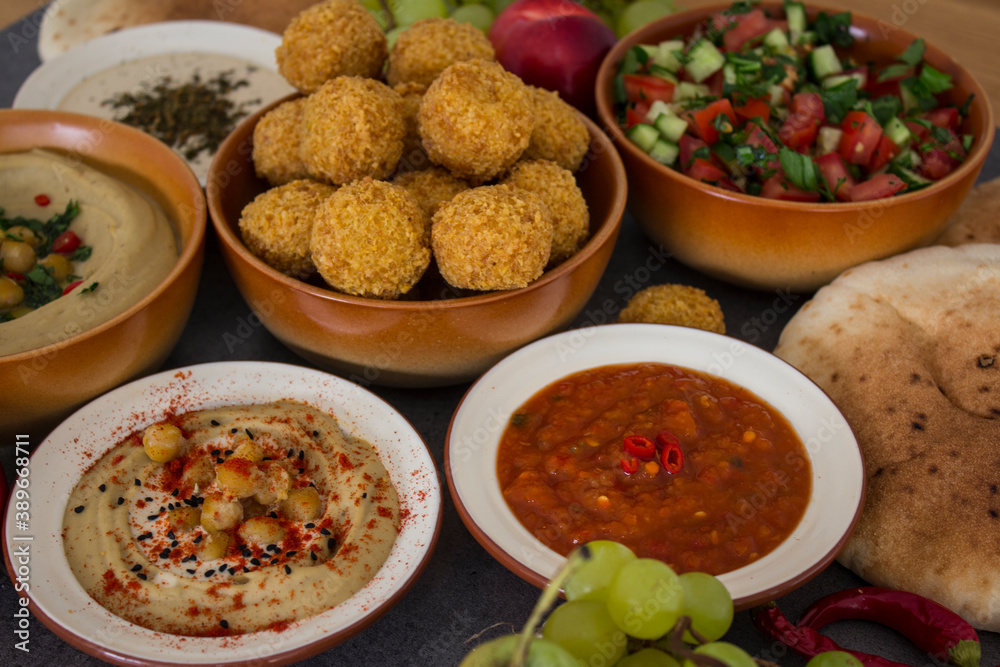 Traditional food of Israel on dark grey background with copy space. Colorful authentic meals top view photo: plate of hummus, falafels, salad, pita bread and tahini sauce. 