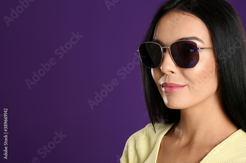 Beautiful woman wearing sunglasses on purple background, closeup. Space for text