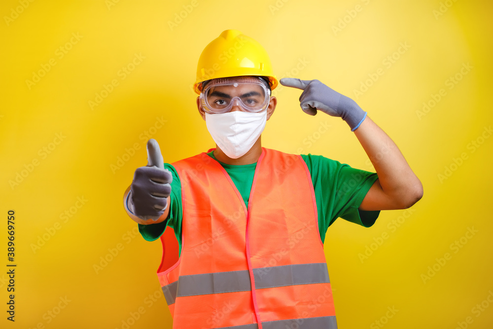 Asian construction worker pointing at his protective mask and savety helmet