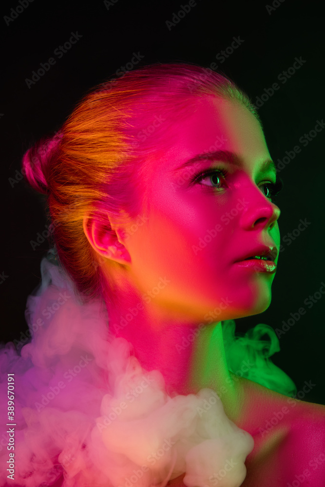 Queen. Portrait of female fashion model in neon light on dark studio background with smoke. Beautiful caucasian woman with trendy make-up and well-kept skin. Vivid style, beauty concept. Close up.