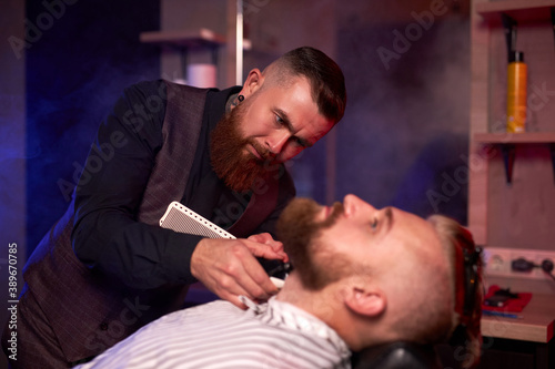 caucasian hipster client man visiting in barber shop shaving beard by professional hairdresser, stylish and and modern beard in salon