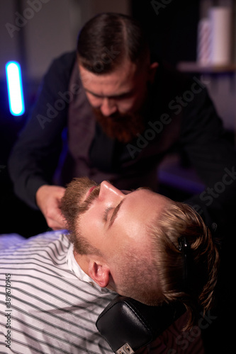 caucasian hipster client man visiting in barber shop shaving beard by professional hairdresser, stylish and and modern beard in salon