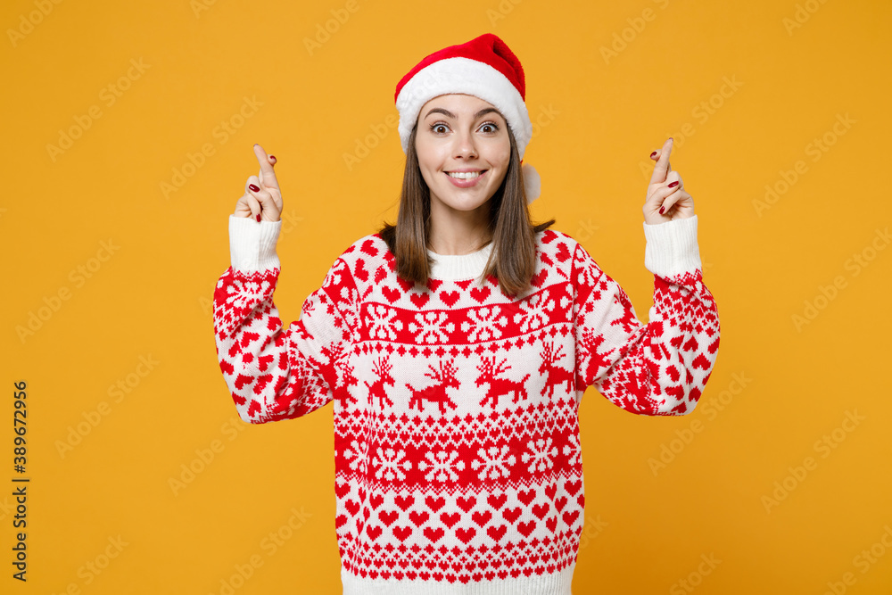 Excited young Santa woman in red sweater Christmas hat waiting for special moment, keeping fingers crossed making wish isolated on yellow background. Happy New Year celebration merry holiday concept. Excited young Santa woman in red sweater Christmas hat waiting for special moment, keeping fingers crossed making wish isolated on yellow background. Happy New Year celebration merry holiday concept.