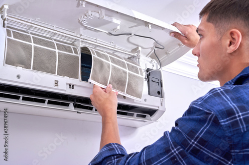 Caucasian male master in blue shirt cleans filters, installs and fixes air conditioner indoors