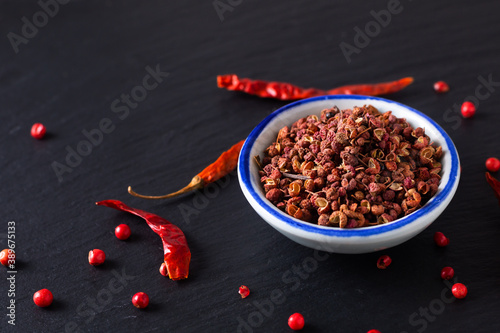 Food hot and spicy ingredients concept Sichuan, Szechuan, Szechwan pepper in small ceramic bowl on black slate stone board with copy space photo