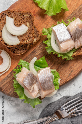 Sandwich with salted herring, rye bread, onions, and lettuce close-up. Scandinavian food.