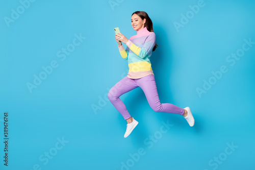 Full length body size view of nice addicted focused cheerful girl jumping using gadget 5g free time isolated on bright blue color background