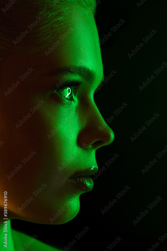 Half. Portrait of female fashion model in neon light on dark studio background. Beautiful caucasian woman with trendy make-up and well-kept skin. Vivid style, beauty concept. Close up.