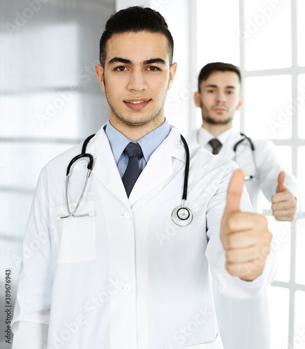 Arab doctor man showing Ok sign with thumbs up with caucasian colleague in medical office or clinic. Diverse doctors team  best treatment  medicine and healthcare concept
