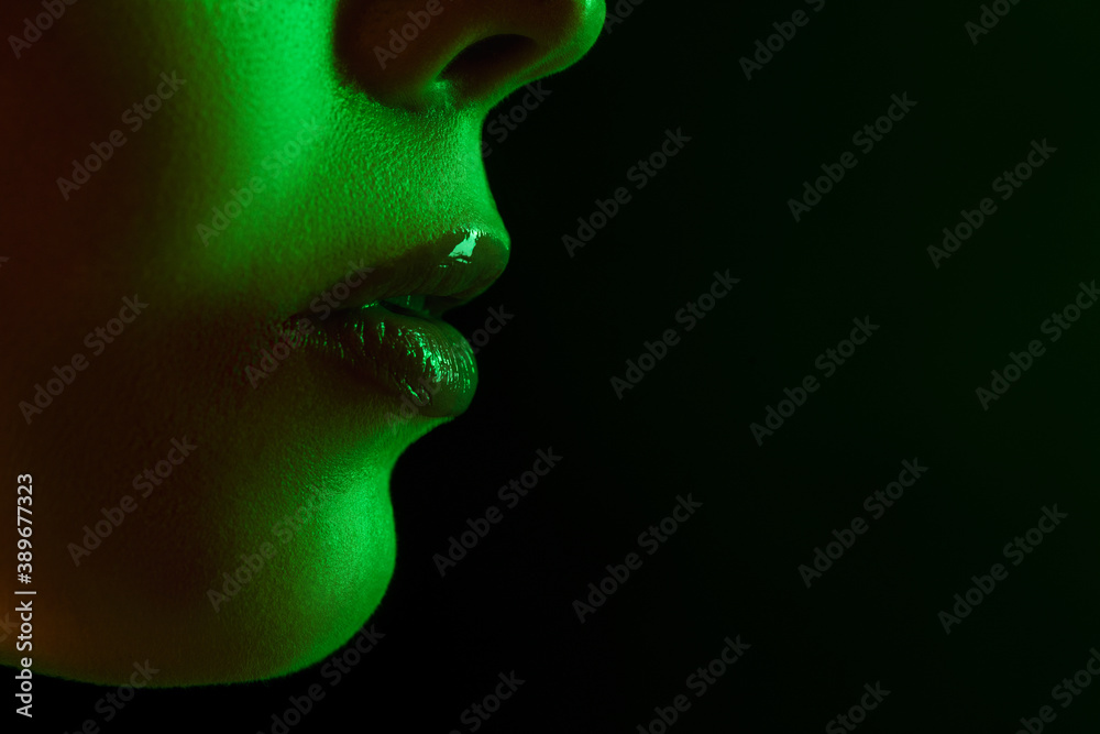 Lips. Portrait of female fashion model in neon light on dark studio background. Beautiful caucasian woman with trendy make-up and well-kept skin. Vivid style, beauty concept. Close up. Flyer