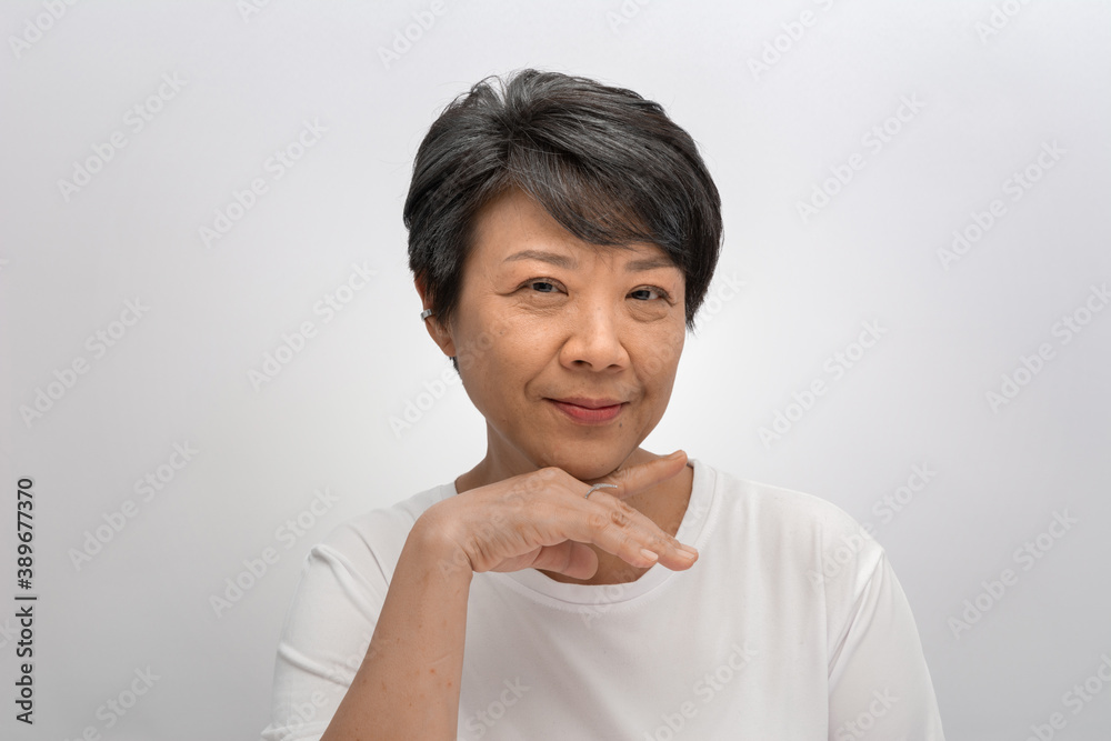 A middle-aged gray-haired Asian woman puts her hand under her chin. And she looks at the camera while smiling, thinking about an idea of the future on a white background, a Beautiful elderly concept A middle-aged gray-haired Asian woman puts her hand under her chin. And she looks at the camera while smiling, thinking about an idea of the future on a white background, a Beautiful elderly concept