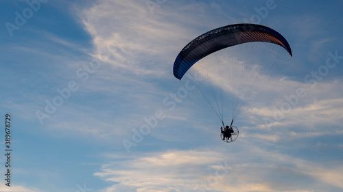 Silhouette of powered paraglider against the blue sky