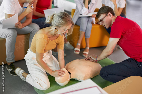 young caucasian female instructor showing how to lay down man during first aid training indoors, isolated in room with group of people