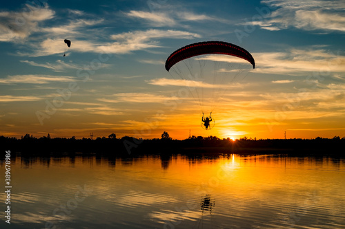 Two powered paragliders flying over the lake during sunset. Silhouetted paramotor pilot with reflection in water photo