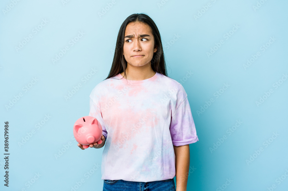 Young asian woman holding a pink bank over isolated background confused, feels doubtful and unsure.