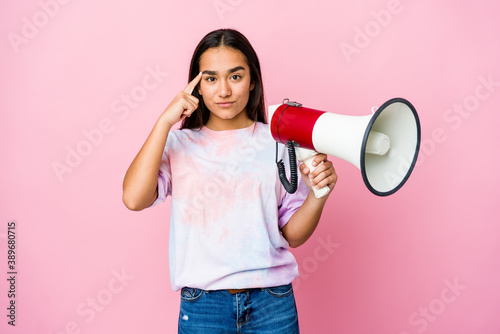 Young asian woman holding a megaphone isolated on pink background pointing temple with finger, thinking, focused on a task.