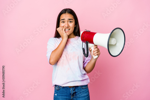 Young asian woman holding a megaphone isolated on pink background biting fingernails, nervous and very anxious.