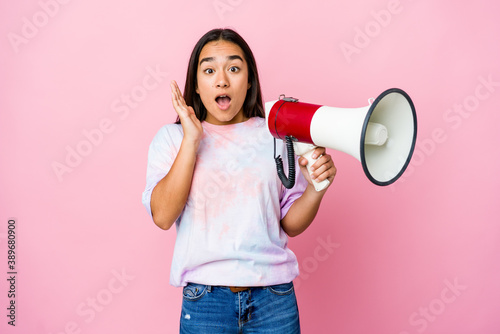 Young asian woman holding a megaphone isolated on pink background surprised and shocked.