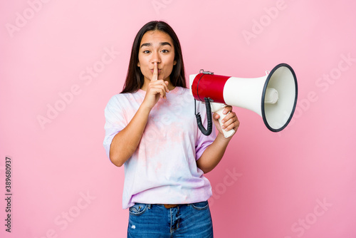 Young asian woman holding a megaphone isolated on pink background keeping a secret or asking for silence.