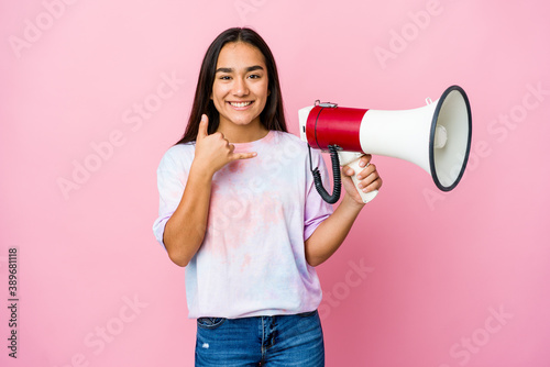 Young asian woman holding a megaphone isolated on pink background showing a mobile phone call gesture with fingers.
