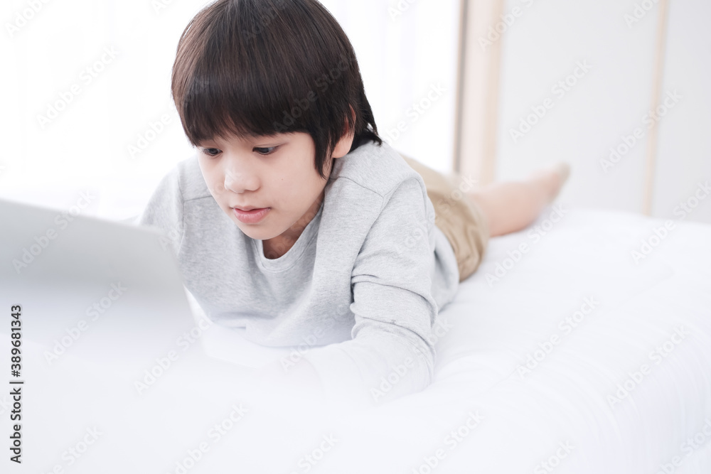 Smiling Asian little boy is studying and doing homework or playing game with laptop in bedroom. Homeschool and quarantine during Covid-19 virus epidemic concept. Distance Learning Online Education Smiling Asian little boy is studying and doing homework or playing game with laptop in bedroom. Homeschool and quarantine during Covid-19 virus epidemic concept. Distance Learning Online Education