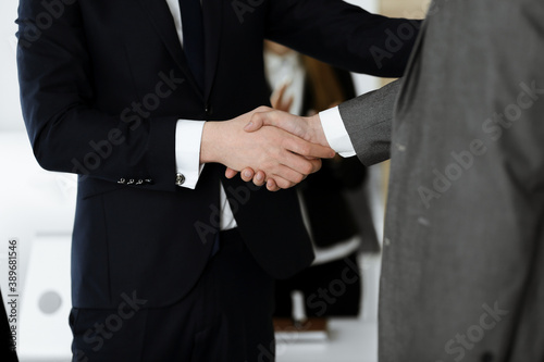 Unknown businessman shaking hands with his colleague or partner while standing straight in modern office, close-up. Business people group at meeting