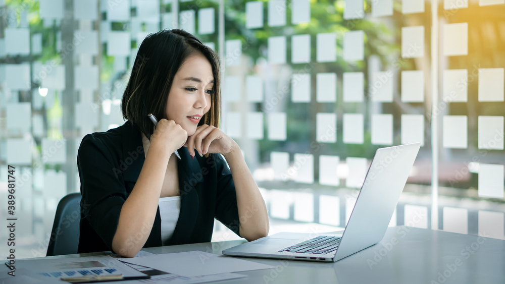 Image of a happy, cheerful, bright, cute, business woman sitting in the office using a laptop computer to work with graphs on the table. Image of a happy, cheerful, bright, cute, business woman sitting in the office using a laptop computer to work with graphs on the table.