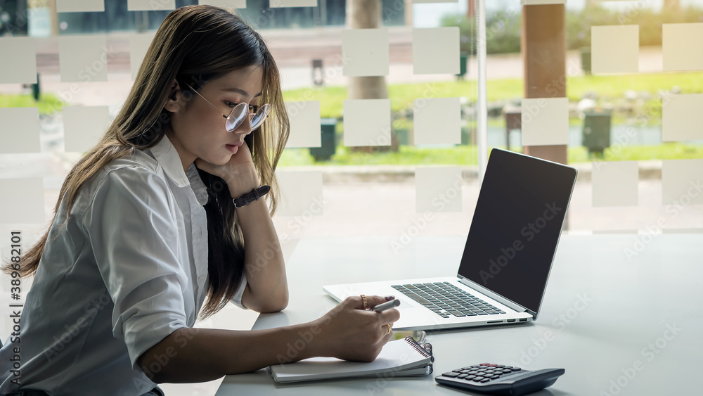 The image of an Asian business woman wearing glasses is working on a laptop computer on an office table. The image of an Asian business woman wearing glasses is working on a laptop computer on an office table.