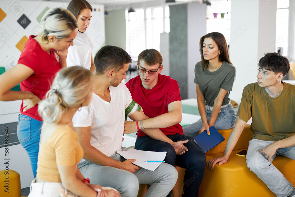man wearing tourniquet on arm of injured person during class of giving first aid, help people. indoors man wearing tourniquet on arm of injured person during class of giving first aid, help people. indoors