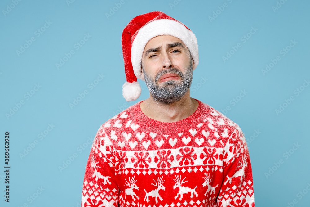 Upset crying Northern bearded man frozen icy snow face in Santa hat Christmas sweater looks camera isolated on blue background in studio. Happy New Year celebration merry holiday winter time concept. Upset crying Northern bearded man frozen icy snow face in Santa hat Christmas sweater looks camera isolated on blue background in studio. Happy New Year celebration merry holiday winter time concept.