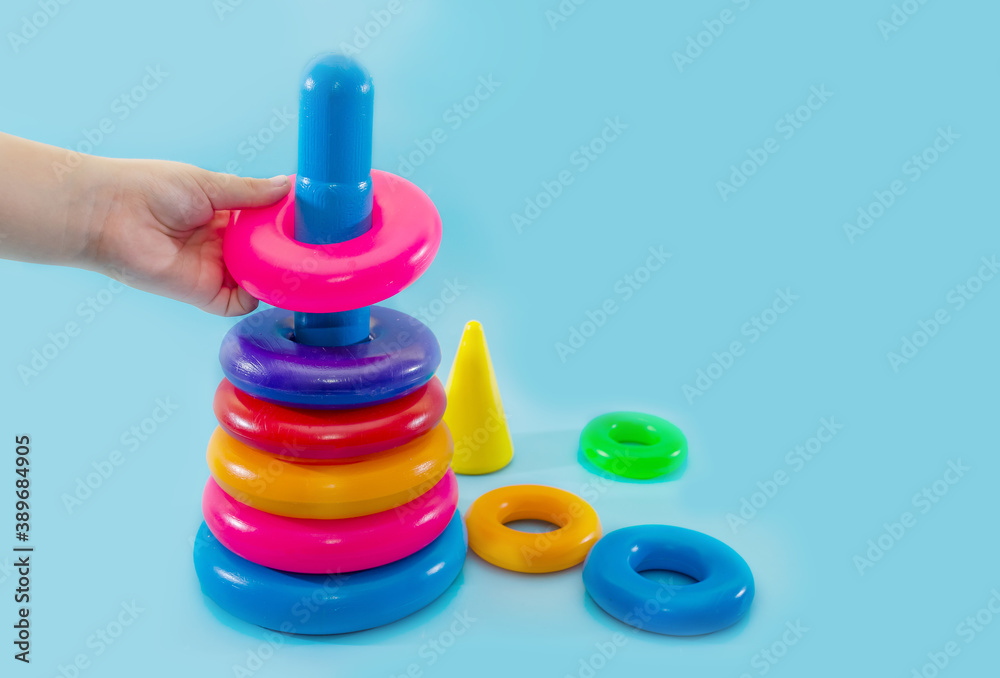 Child's hand folds multi-colored pyramid isolated on blue background.Close-up of a child's hand playing with a toy pyramid. Child's hand folds multi-colored pyramid isolated on blue background.Close-up of a child's hand playing with a toy pyramid.